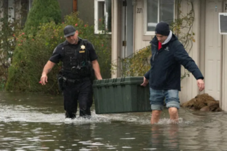 A sheriff helps a resident carry a storage bin through rising floodwater in a residential neighborhood during severe Pacific Northwest flooding.
